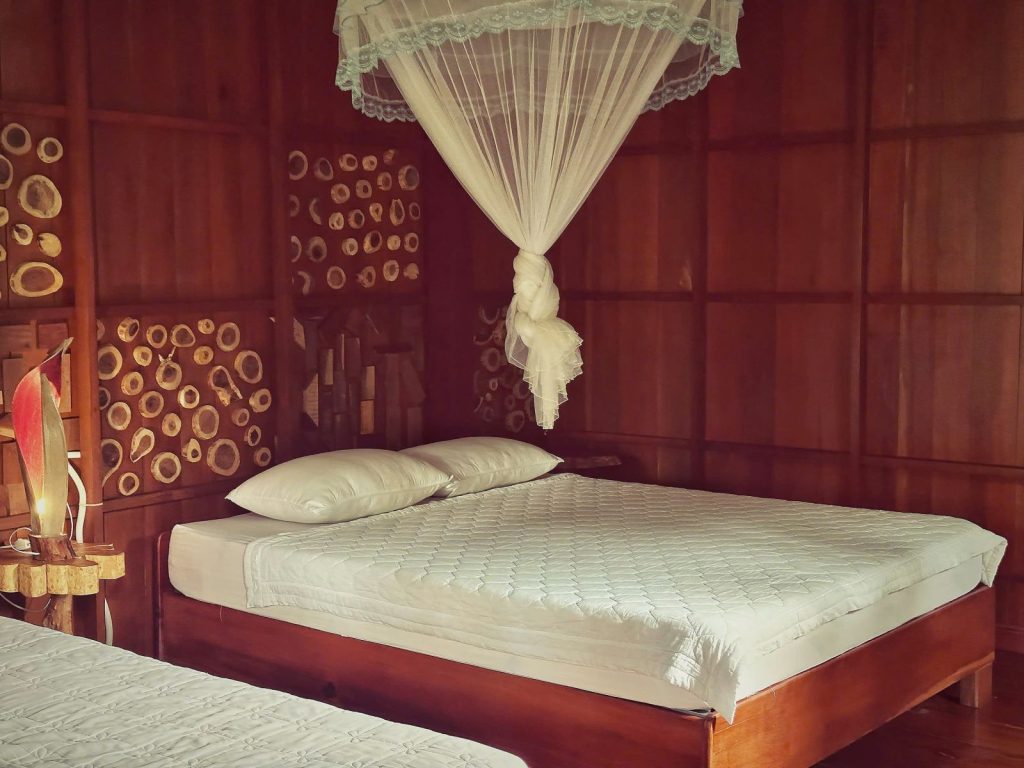 A wooden bedroom with two beds and a white mosquito net tied up above.