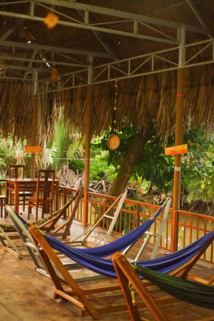 Hammocks strung under a large thatched pavilion with tables and lanterns.