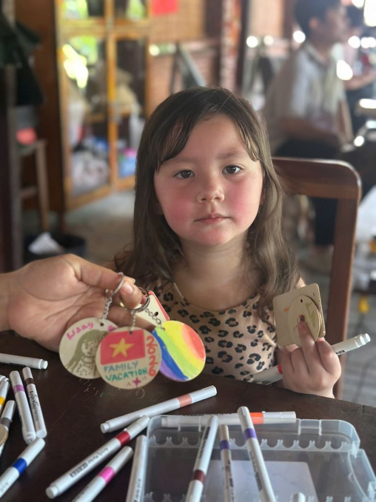 A girl at a table of marker pens, next to hand-painted wooden keyrings.