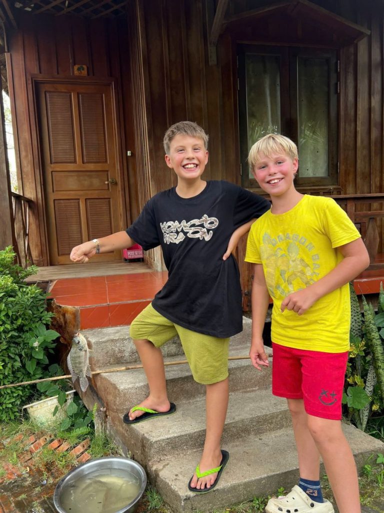 Two boys in black and yellow T-shirts standing arm in arm by a wooden cottage door.