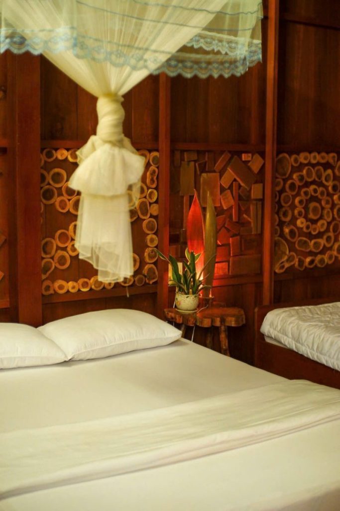 A white bed beneath a knotted mosquito net in a wooden room.