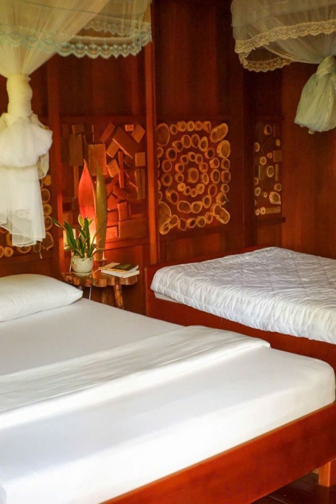 Two single beds with tied-back nets in a warmly lit wooden room.