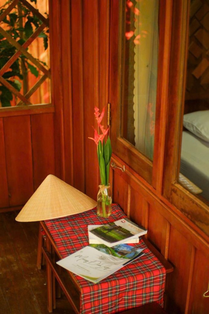 A conical hat and books on a red checked table by a wooden window.