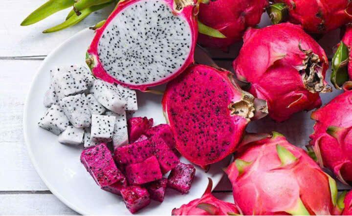 Dragon fruit with red and white flesh, whole and cut into cubes on a plate.