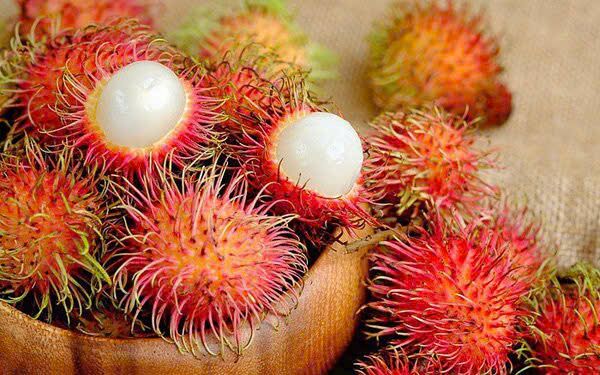 Hairy red rambutans in a wooden bowl, two opened to show the white fruit.