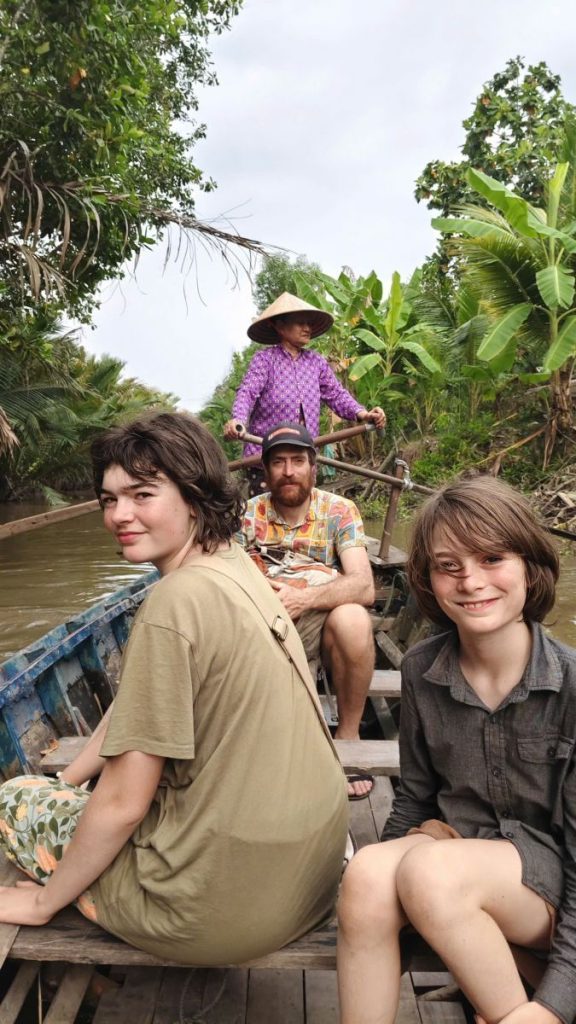 Two young guests smiling in a boat rowed by a woman in a conical hat.