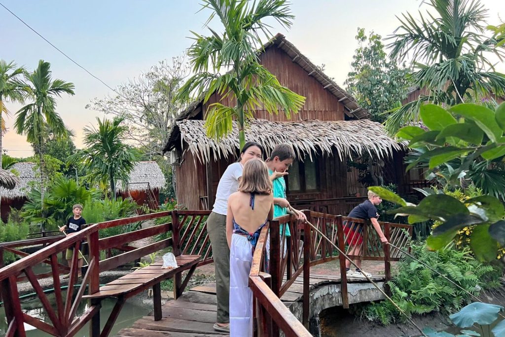 Guests on the wooden bridge by a thatched bungalow.