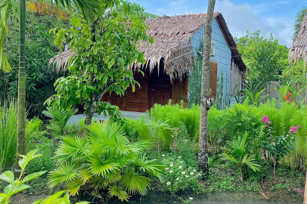 Thatched bungalow behind a lush tropical garden.