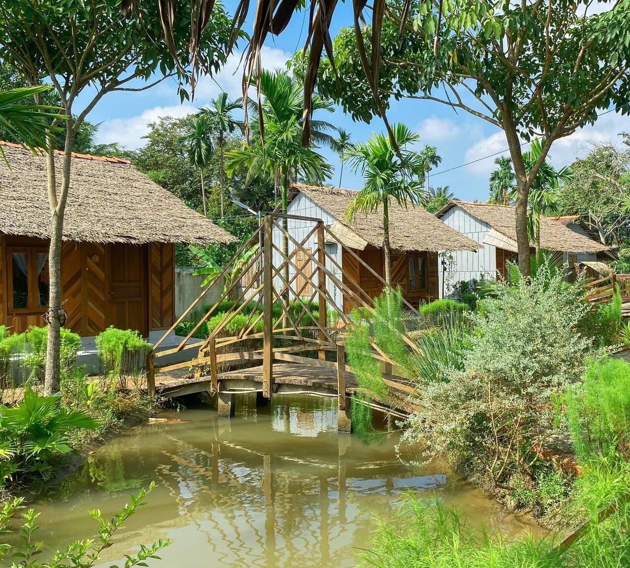 Thatched bungalows and a wooden footbridge at Mương Đình Lodge.