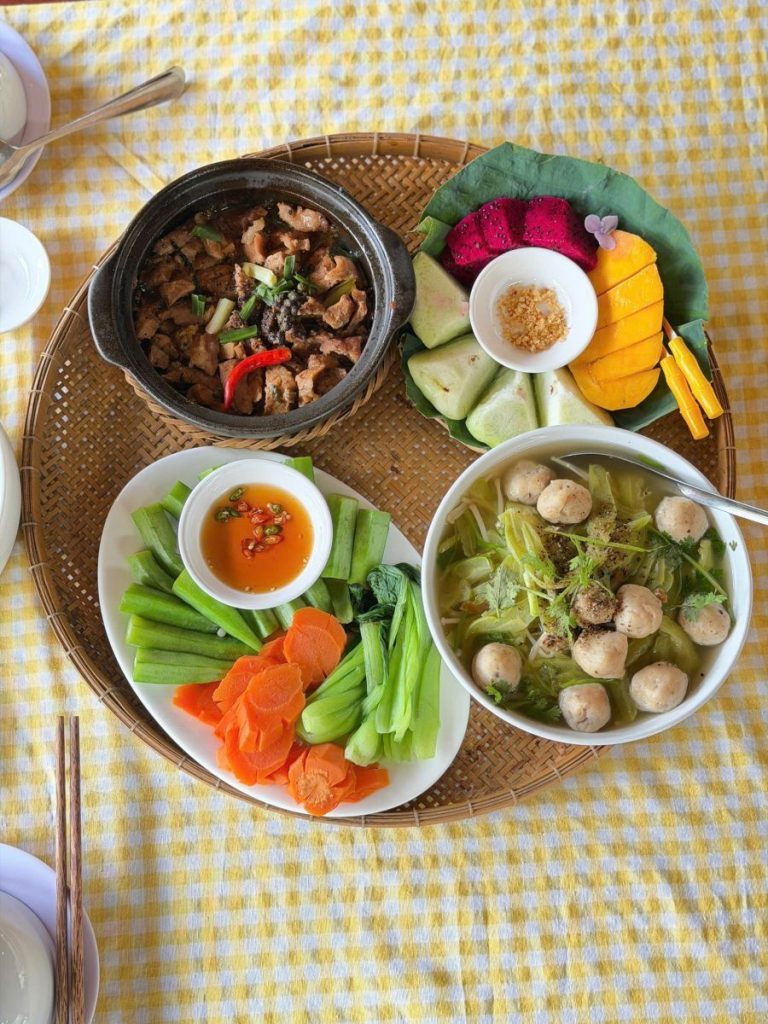 A tray of clay pot stew, meatball soup, vegetables and fruit, from above.