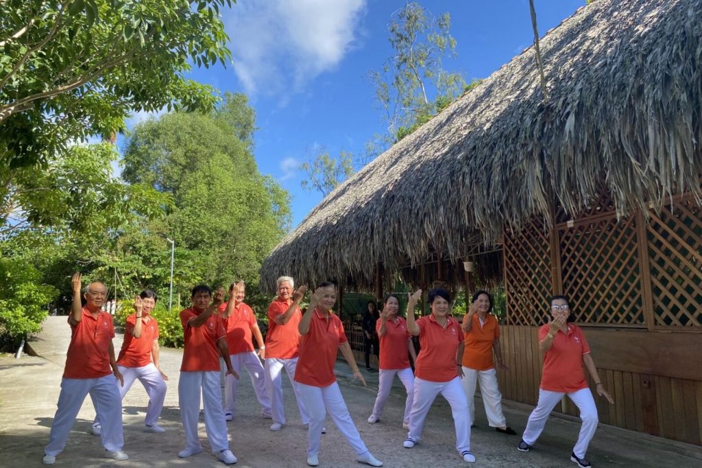 A group exercising in matching shirts beside a thatched pavilion.
