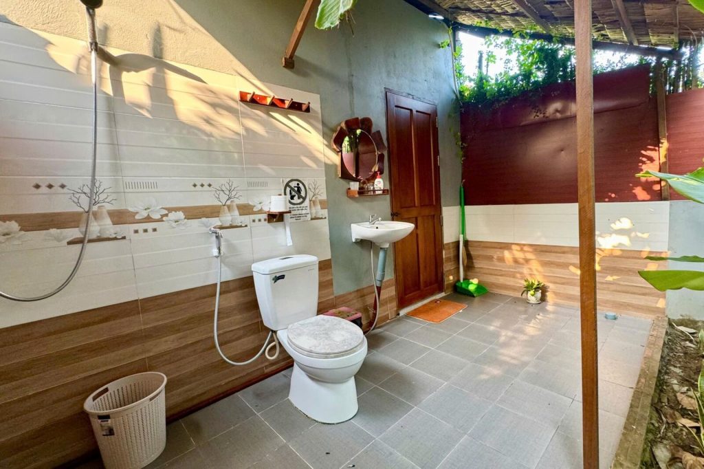Open-air bathroom with shower and garden plants.