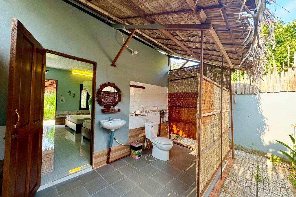 Open-air bathroom with tiled floor and round mirror.
