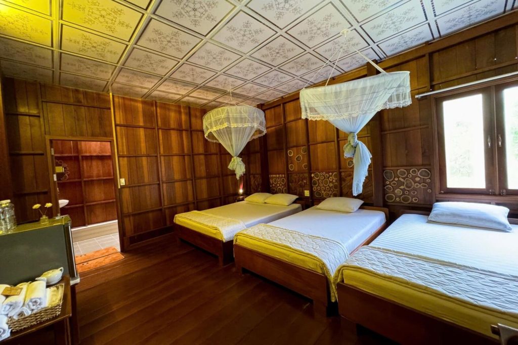 A wooden family room with three beds and mosquito nets.