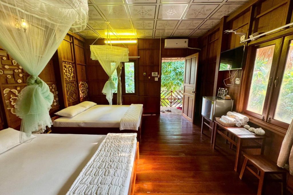 Wooden room with beds, mosquito nets and desk.